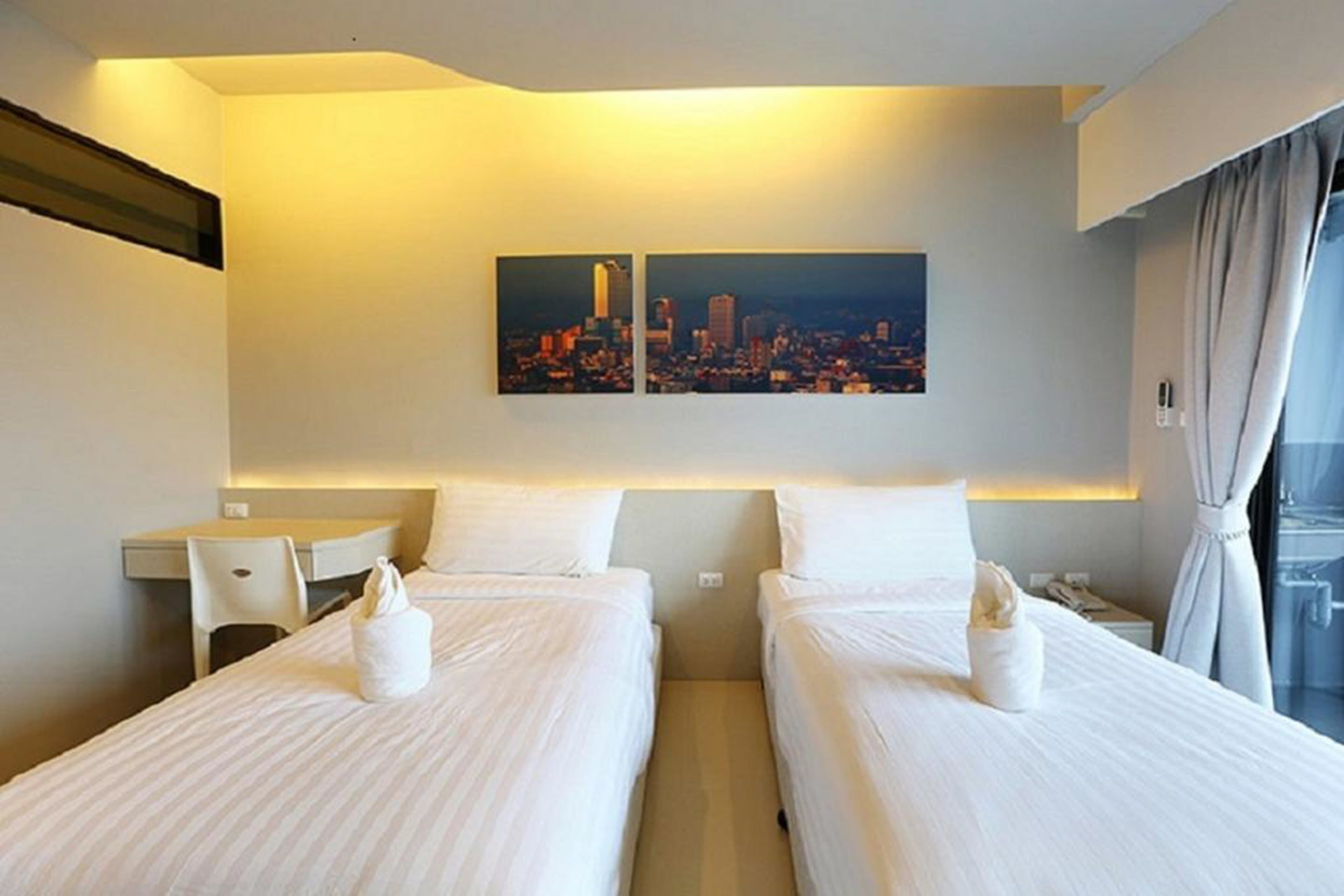 Une chambre d’hôtel avec deux lits, un bureau et un tableau représentant un paysage urbain accroché au mur.