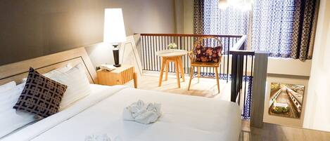 A hotel room with a bed, a nightstand, a lamp, a chair, a small table, and a balcony with patterned curtains.