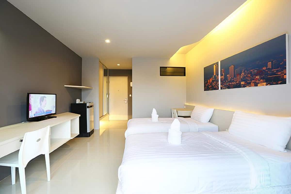 A modern hotel room with a large bed, a desk with a computer, and a cityscape painting on the wall.