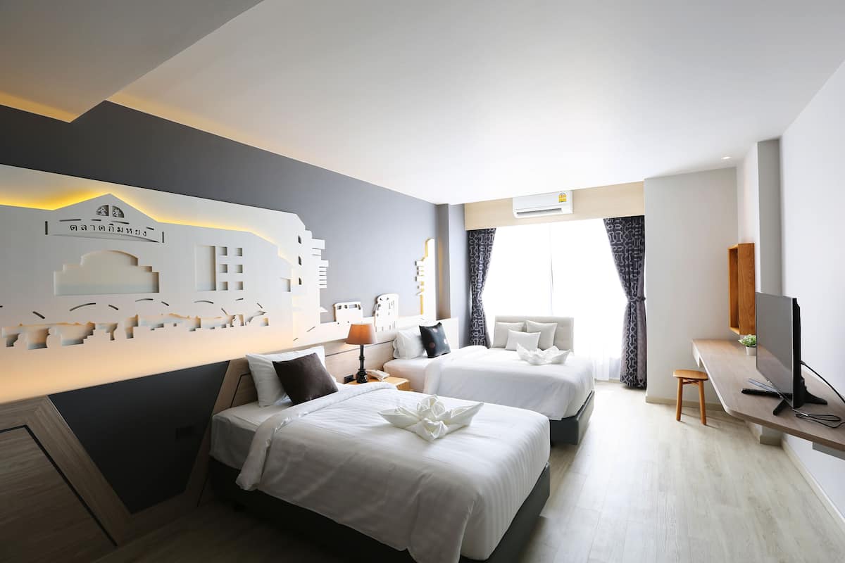 A hotel room with two beds, a desk with a TV, and a decorative wall piece.