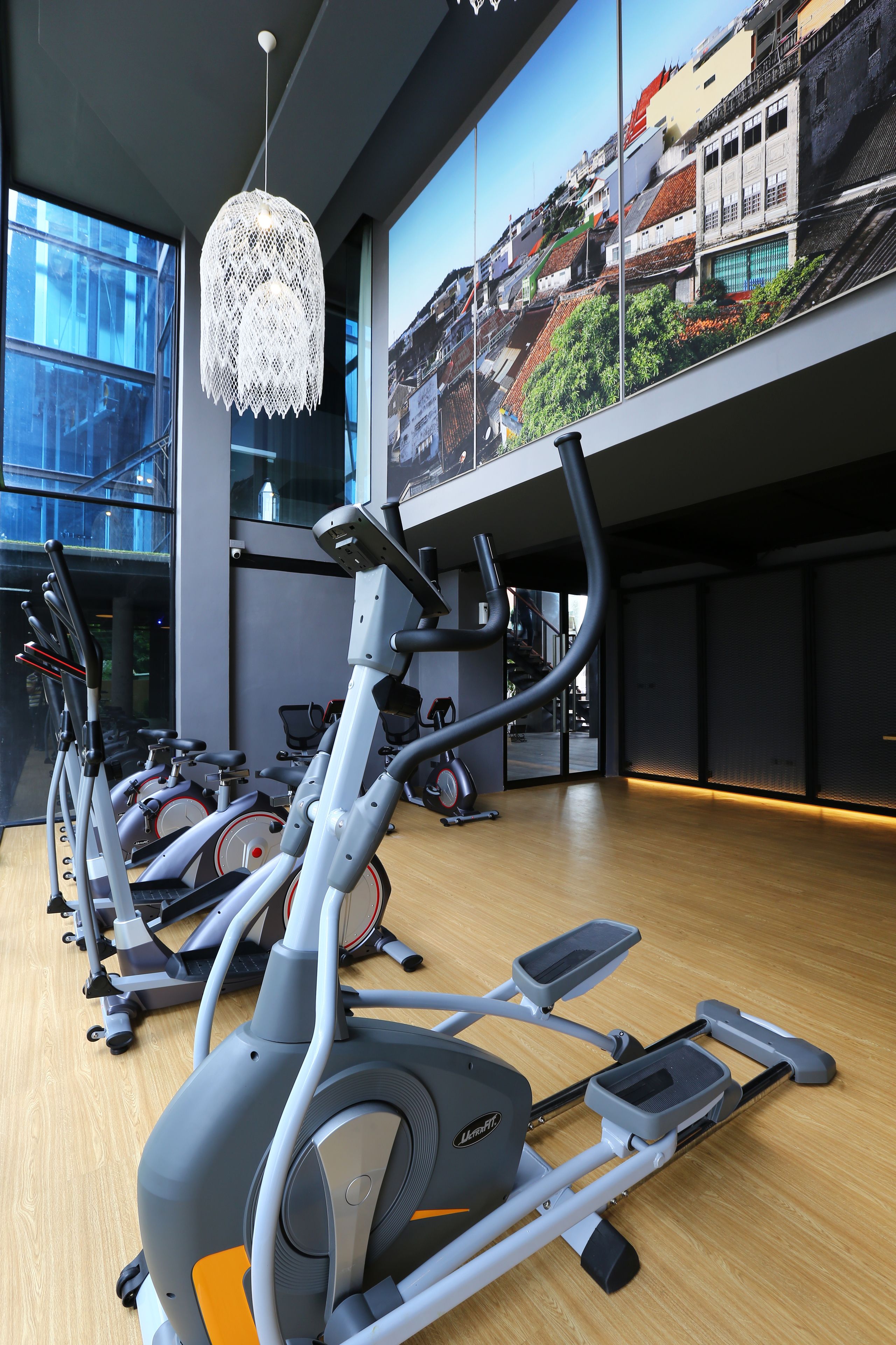 Un gimnasio con equipamiento de ejercicio, ventanas amplias y vista panorámica de la ciudad.