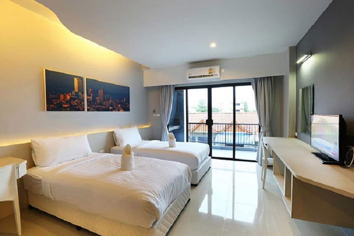 A hotel room with two beds, a desk, a television, and a cityscape painting.