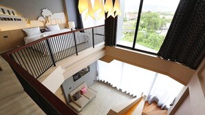 A spacious living area with a high ceiling, a staircase leading to an upper floor, and a large window offering a view of greenery outside. - Hatyai Signature Hotel (Hat Yai)