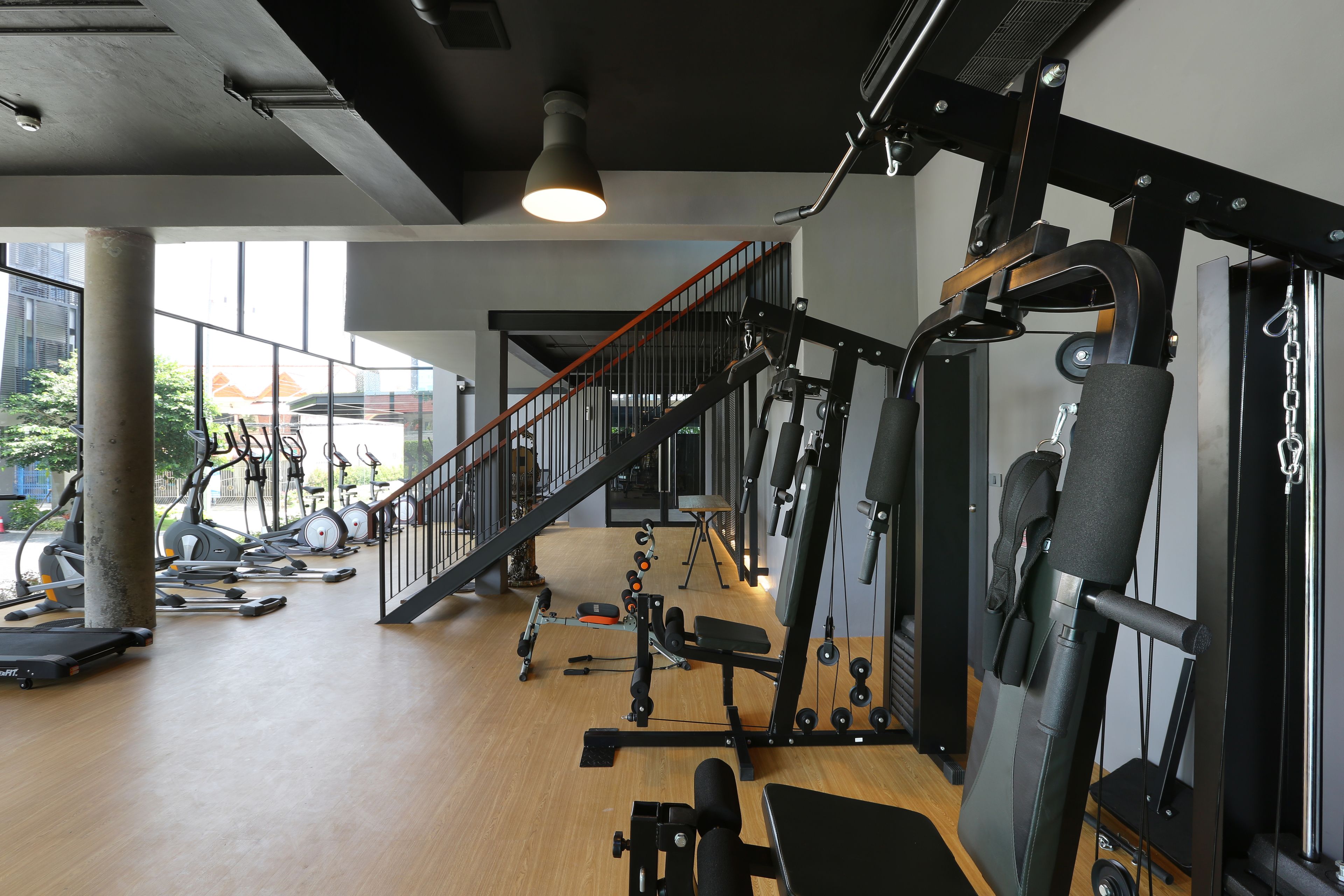 A gym with various exercise equipment, a staircase, and large windows.