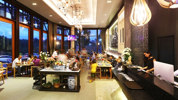 A modern restaurant with large windows, a central dining area, and a reception desk with a computer. - Hatyai Signature Hotel (Hat Yai)