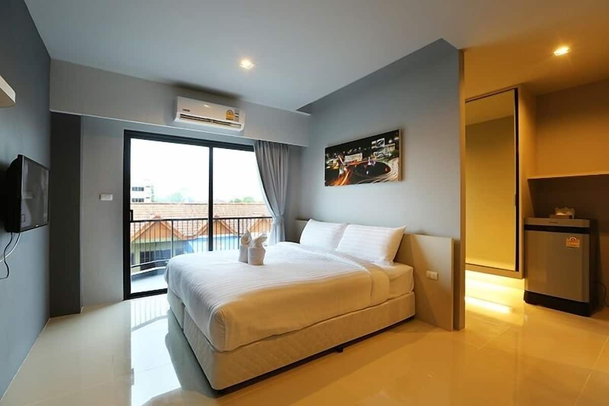 A modern hotel room with a large bed, a flat-screen TV, a balcony with a view, and a small refrigerator.