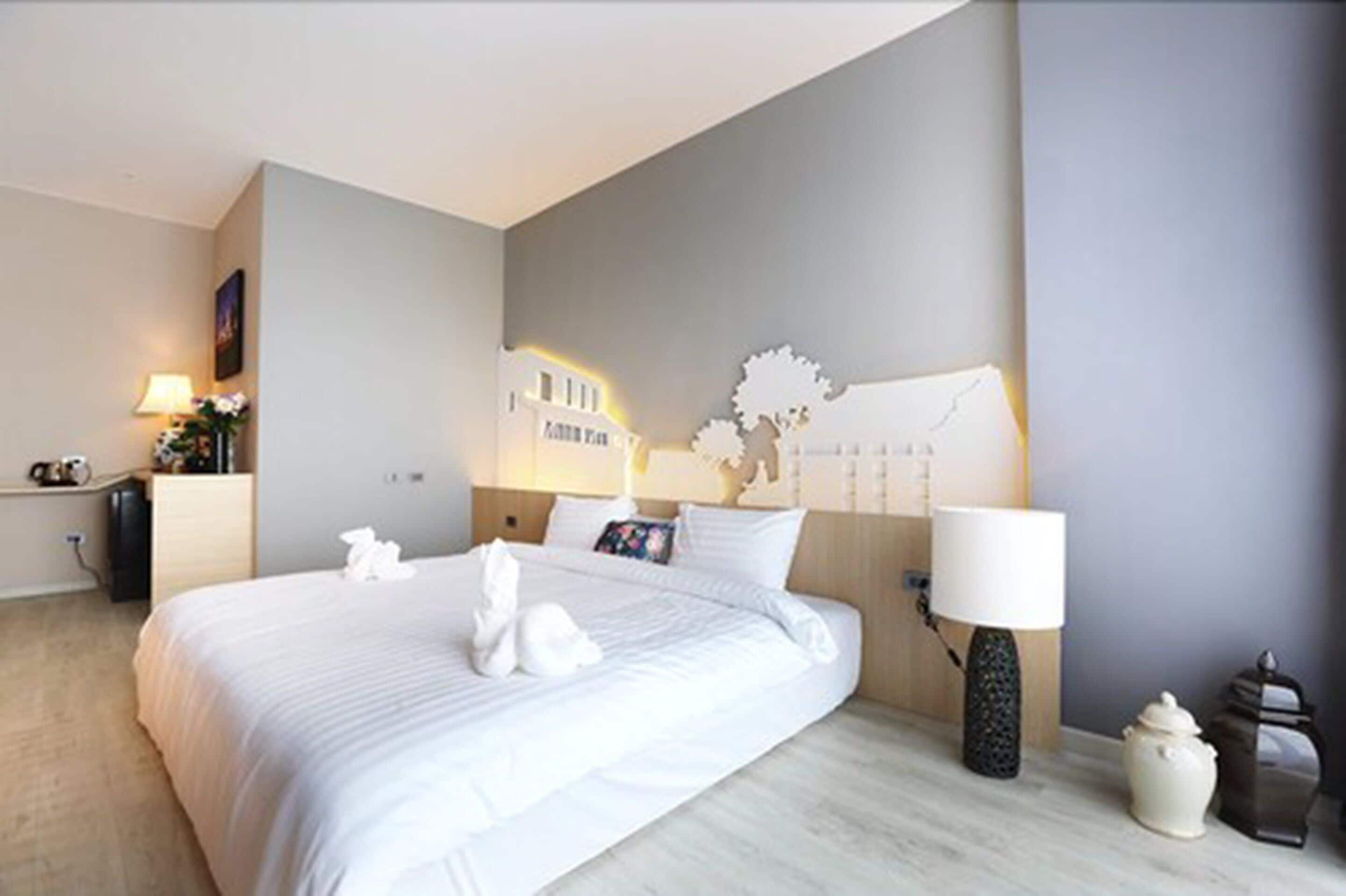 Ein modernes Hotelzimmer mit einem großen Bett, einem Nachttisch mit Lampe, einer Wanddekoration und einem kleinen Schrank.