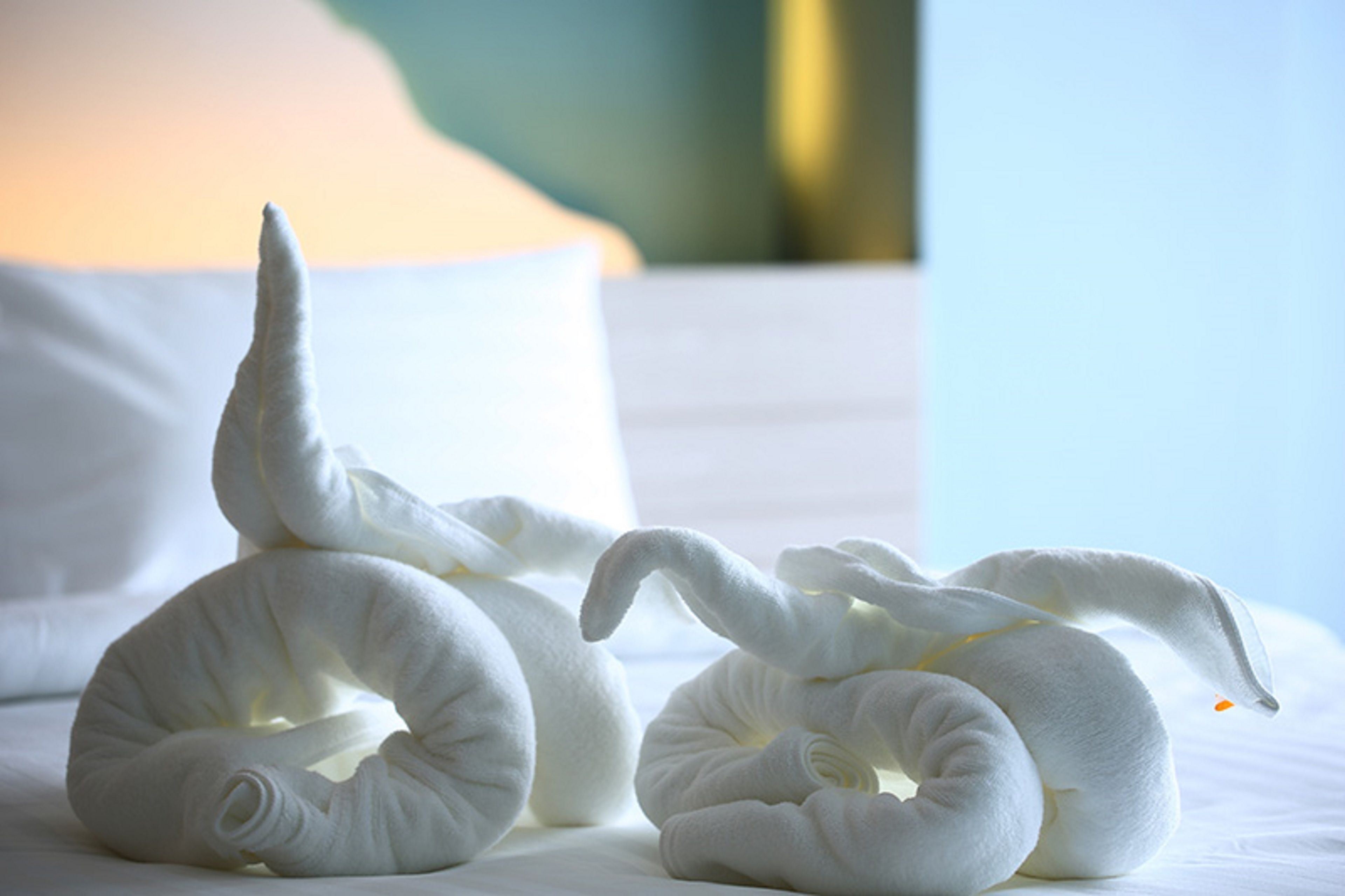 Un lit bien fait, avec du linge de lit blanc et deux cygnes décoratifs faits à partir de serviettes.