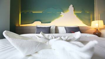 A neatly made bed with white linens and a folded white towel, a lamp on the bedside table, and a wall with a silhouette artwork.