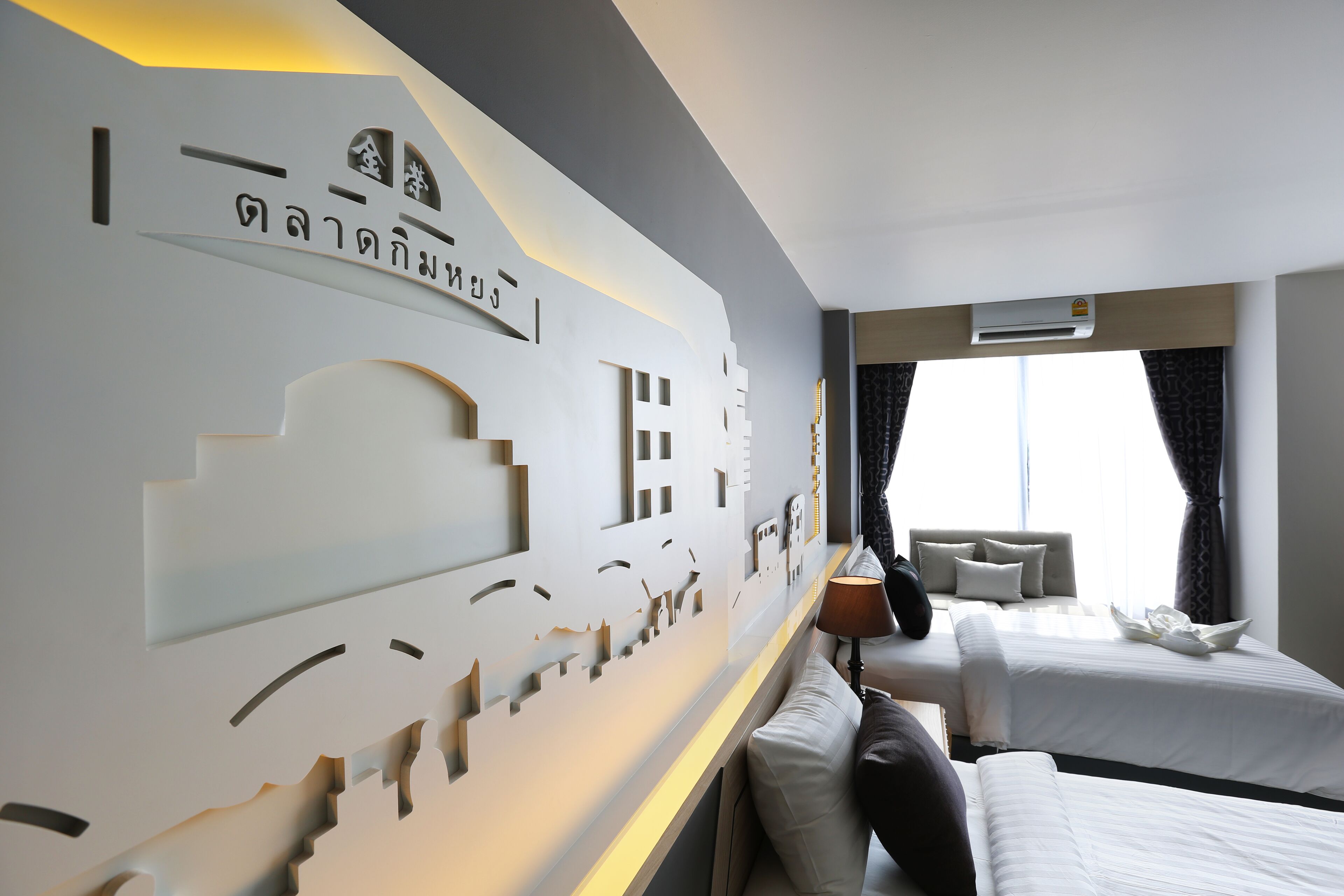 A hotel room with two beds, a wall with a geometric design, and a window with curtains.