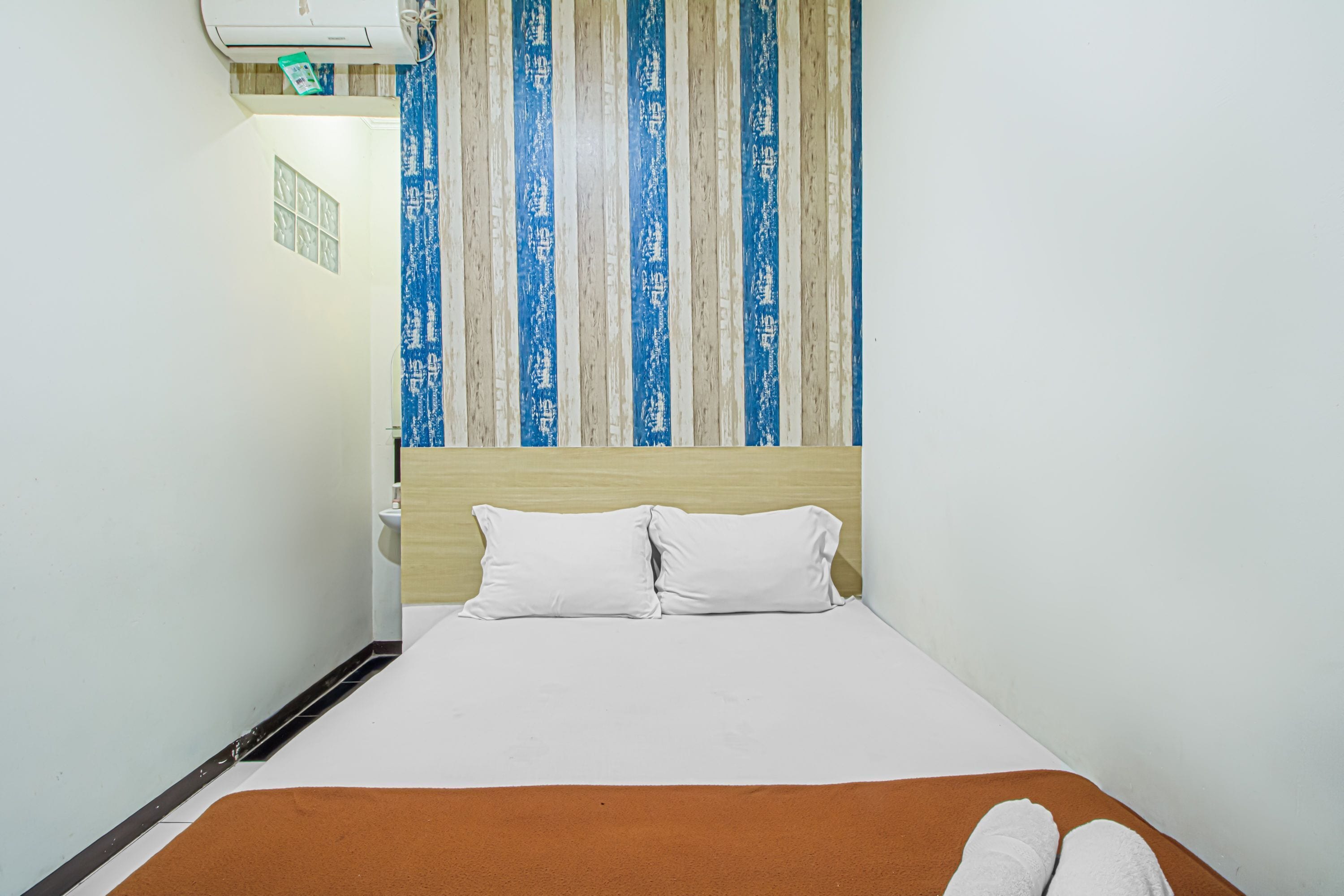 Une chambre d’hôtel avec un lit, des oreillers blancs, un tapis marron et une fenêtre avec des rideaux à rayures.