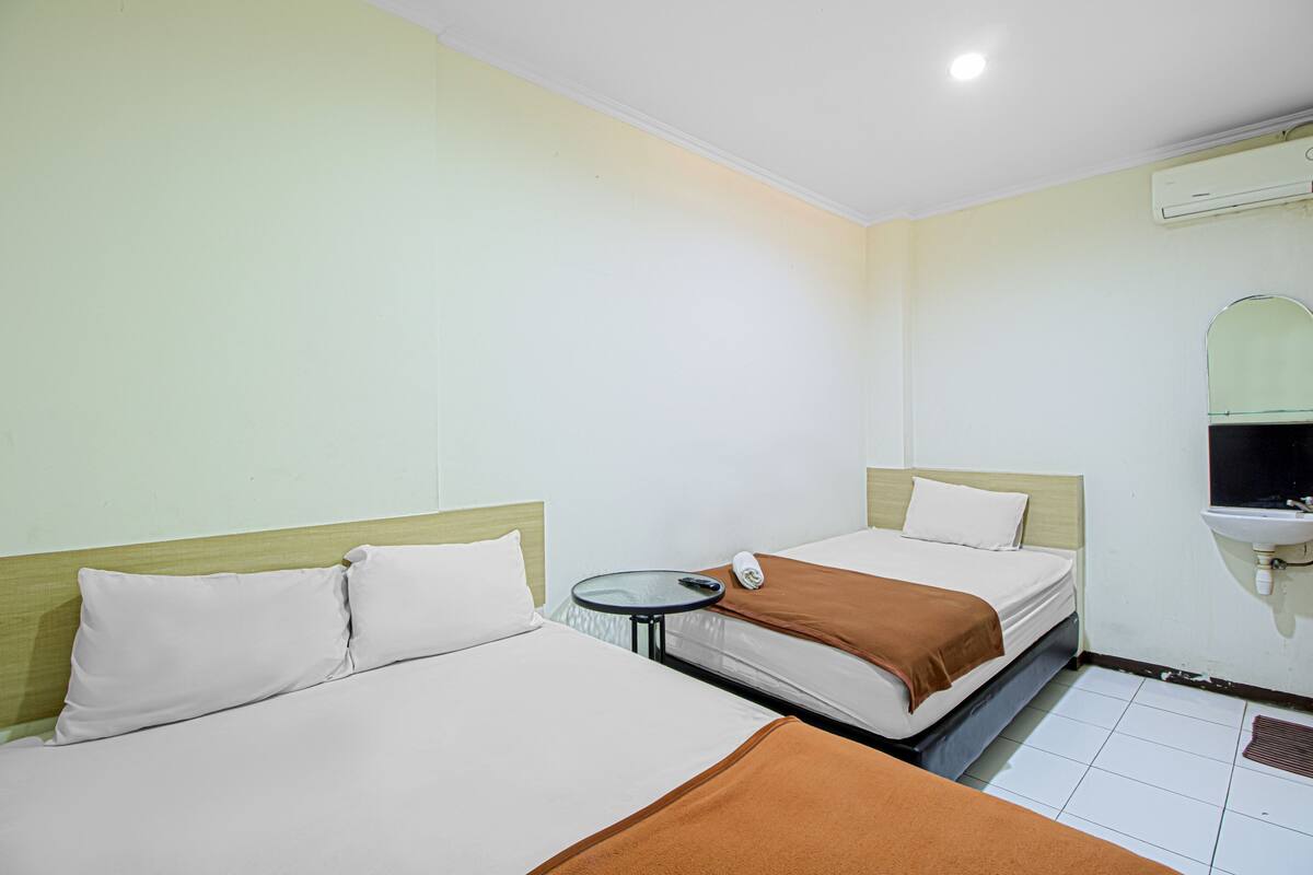 Ein Hotelzimmer mit zwei Betten, einem kleinen runden Tisch, einem wandmontierten Waschbecken und einer Klimaanlage.