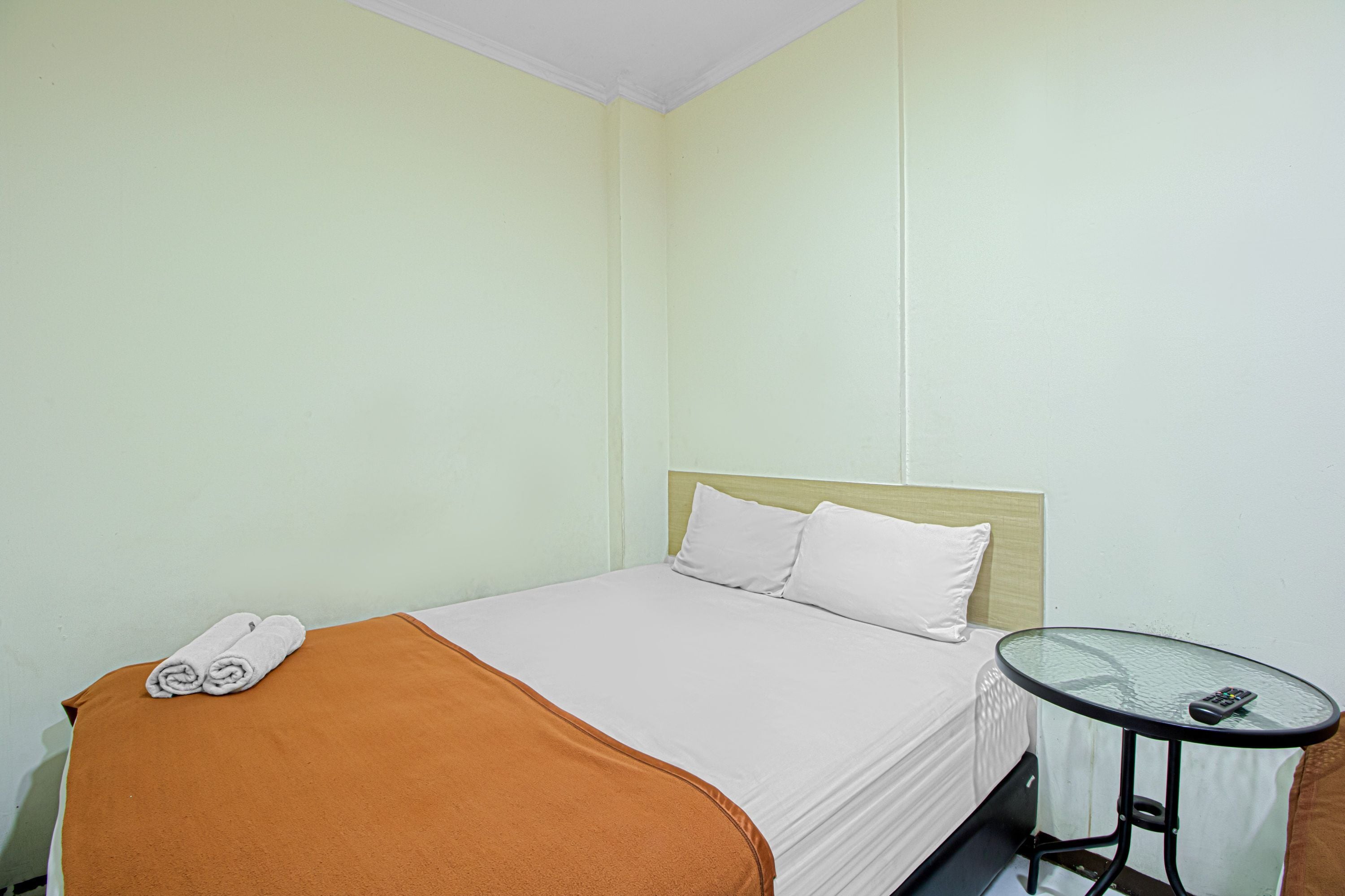 A hotel room with a bed, a glass table, and a remote control on the table.