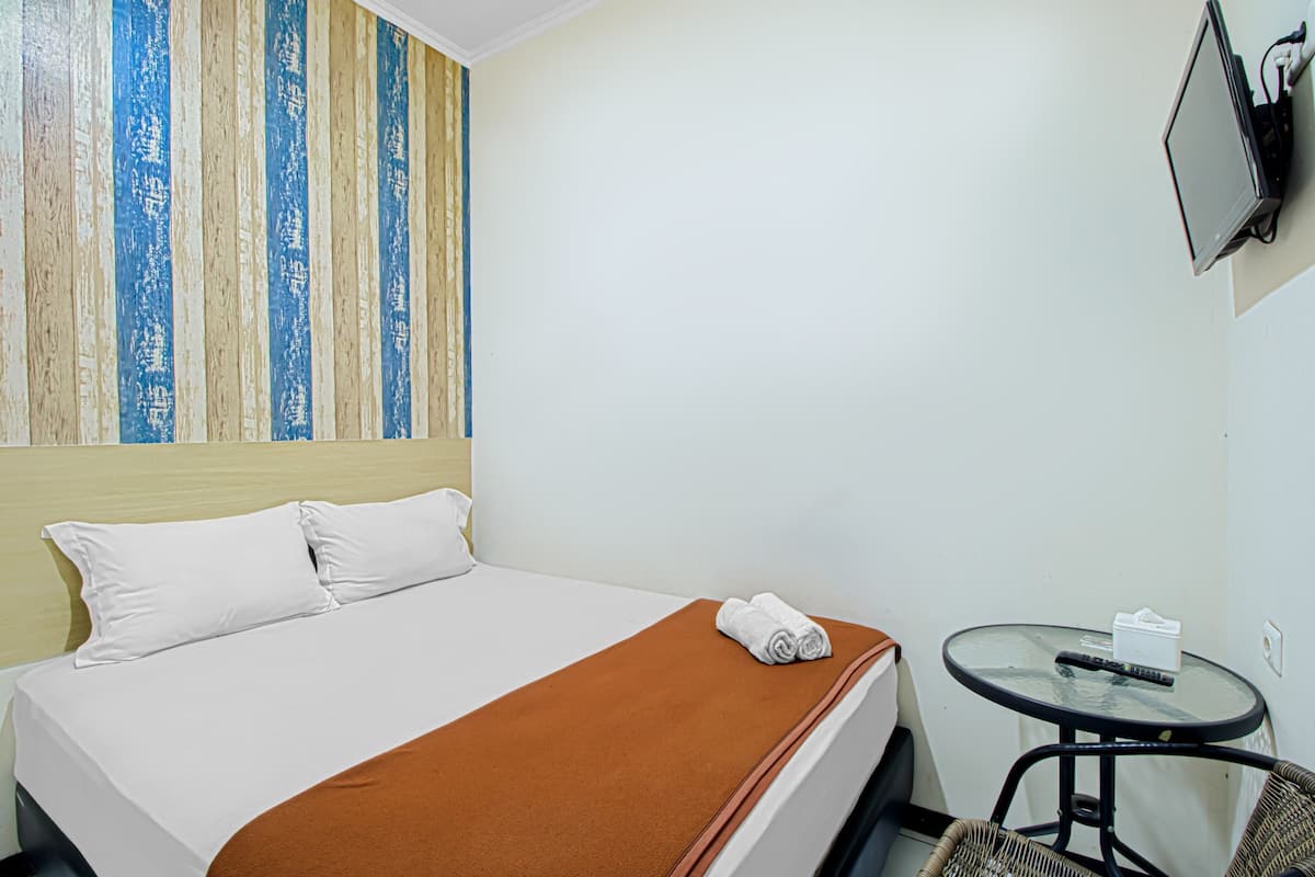 Ein Hotelzimmer mit Bett, einem kleinen runden Tisch mit Stuhl, einem an der Wand montierten Fernseher und einer gestreiften Wanddekoration.