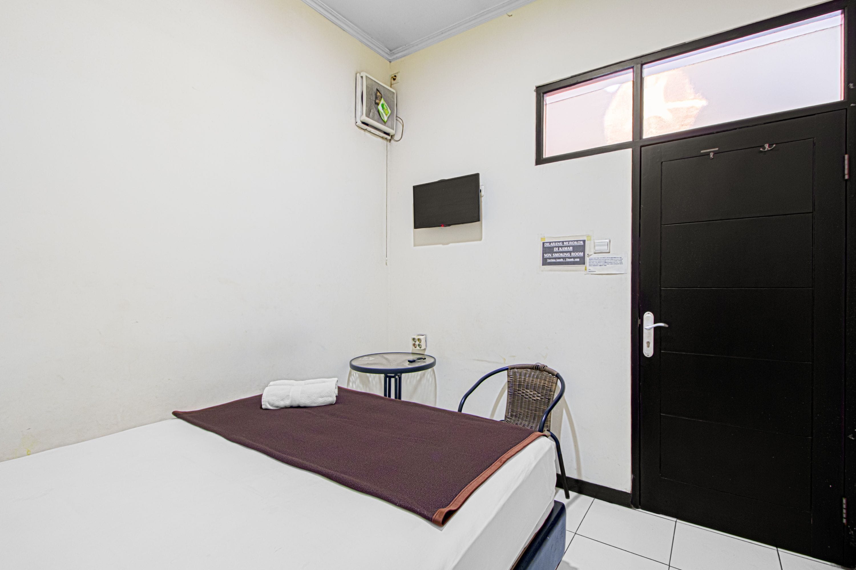 A hotel room with a bed, a small table, a chair, a TV, a door, and a wall-mounted air conditioner.