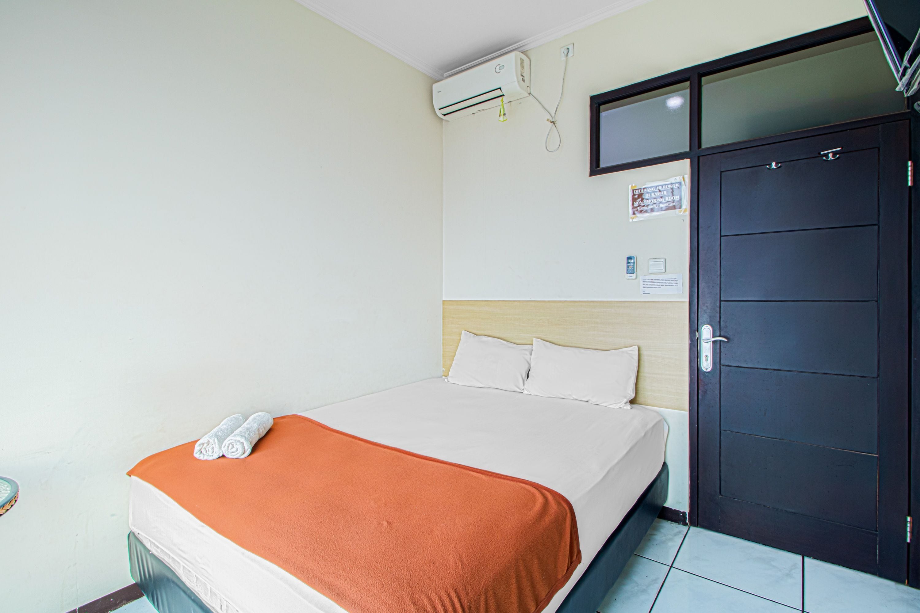 A hotel room with a bed, an air conditioning unit, a door, and a wall-mounted television.