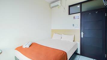 A hotel room with a bed, an air conditioning unit, a door, and a wall-mounted television.