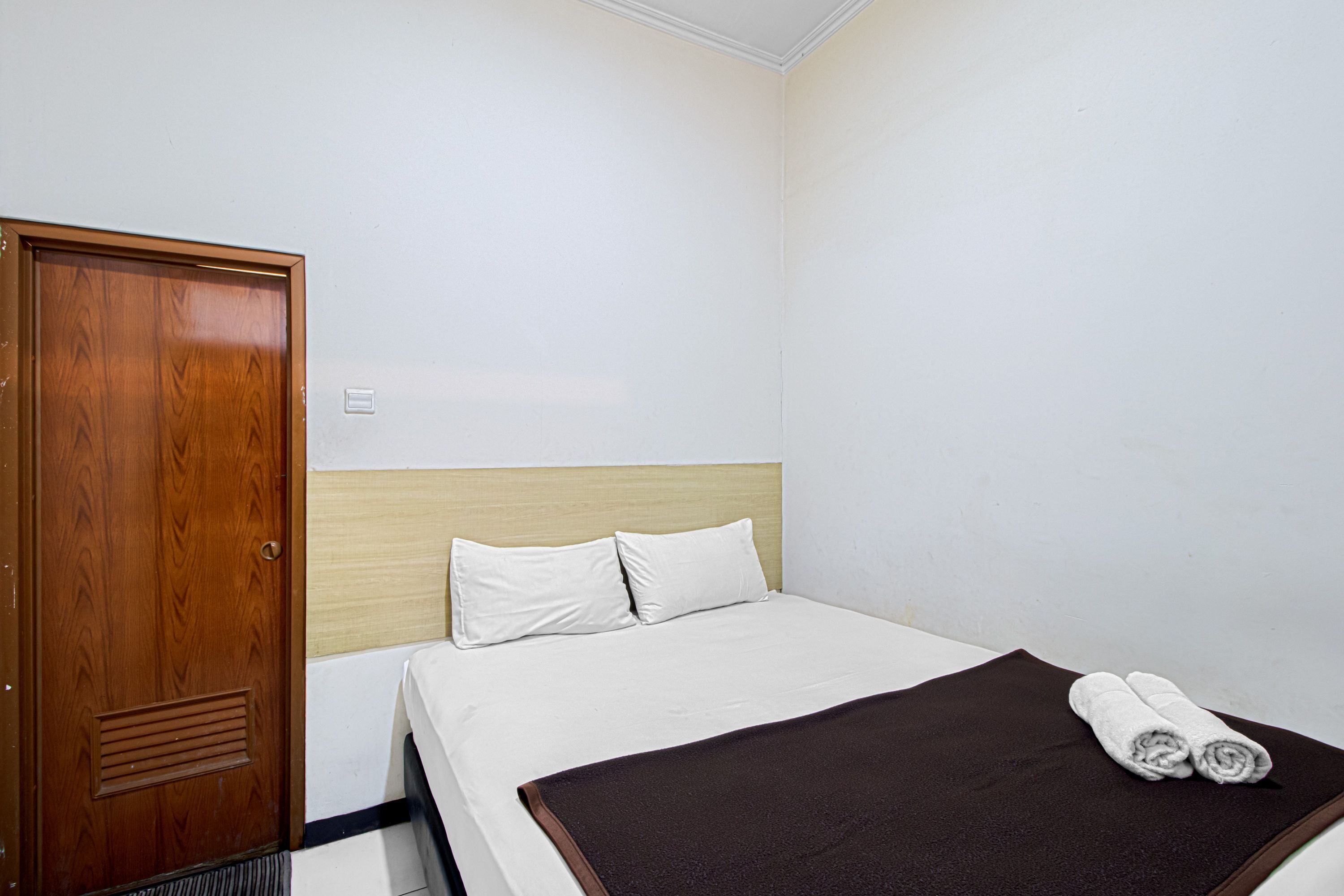A hotel room with a wooden wardrobe, a bed with white bedding, and a brown throw blanket.
