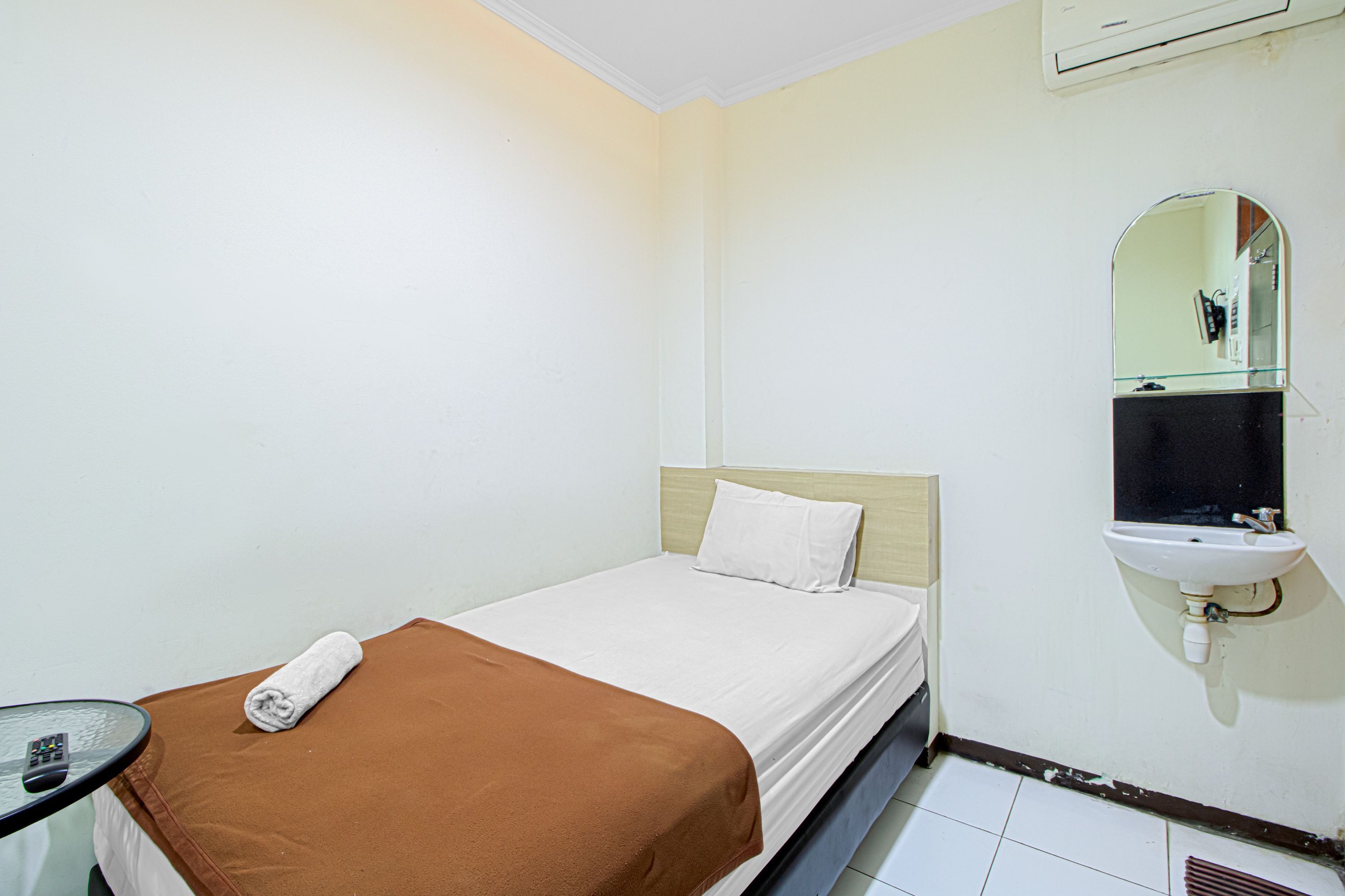 Une chambre d’hôtel avec un lit simple, une table de chevet, un miroir et un lavabo.