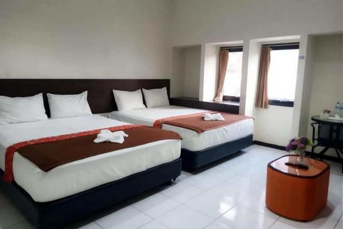 A hotel room with two beds, a small table, and a window with curtains.