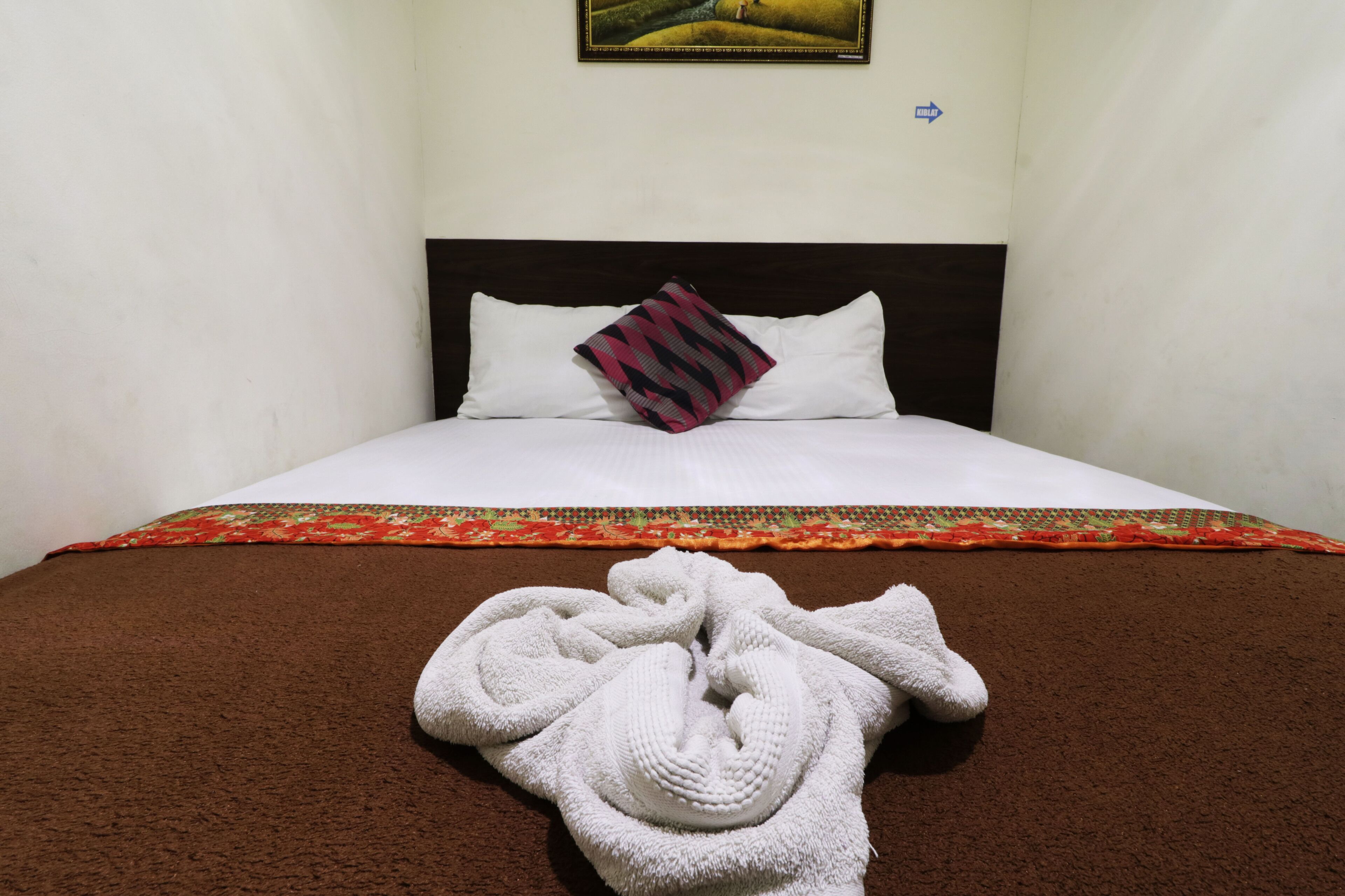 A neatly made bed with white linens, a brown blanket, and a patterned pillow.