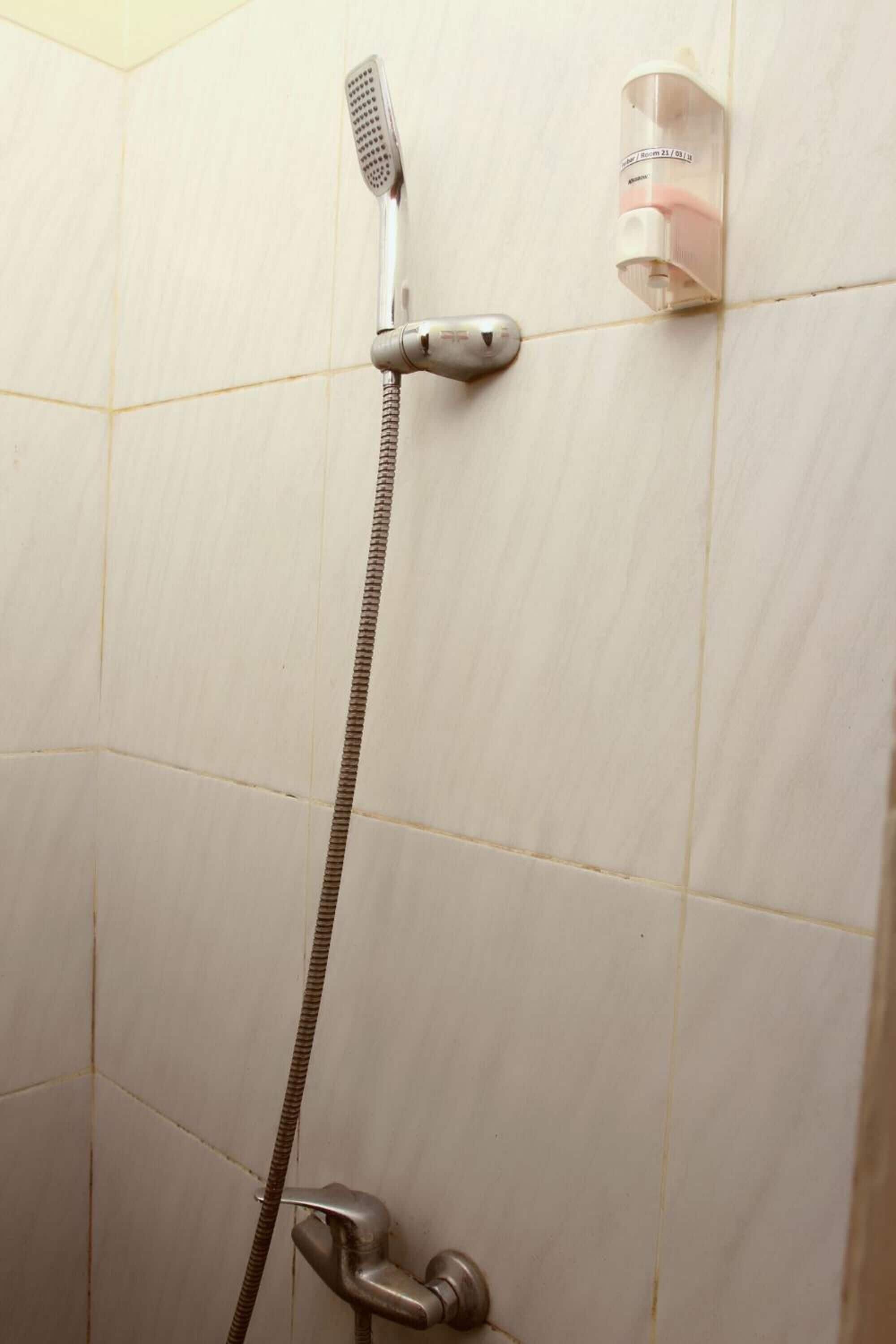 A shower with a handheld showerhead and a wall-mounted soap dispenser.