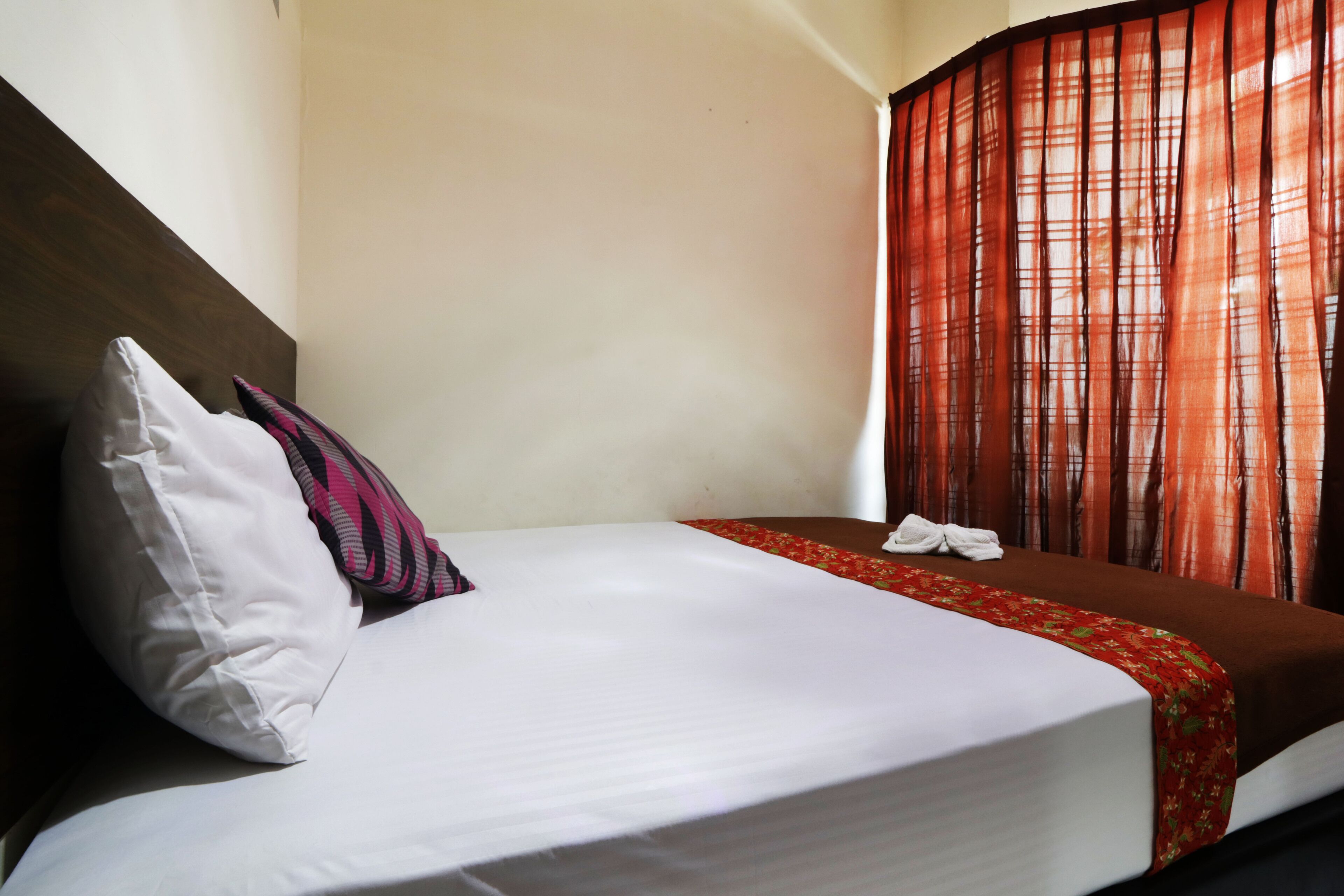 A neatly made bed with a white and red bedspread, a white pillow, and a striped pillow.