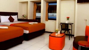 A hotel room with two beds, a small table, a chair, and a view of the city. - Bantal Guling Pasar Baru Bandung (Bandung)