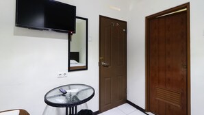 A room with a mounted flat-screen TV, a round glass table with a black bag, a wooden door, and a mirror on the wall. - Bantal Guling Pasar Baru Bandung (Bandung)