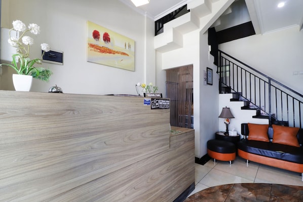 Zona de recepción con mostrador de madera, planta en maceta, un cuadro, una escalera y un sofá.