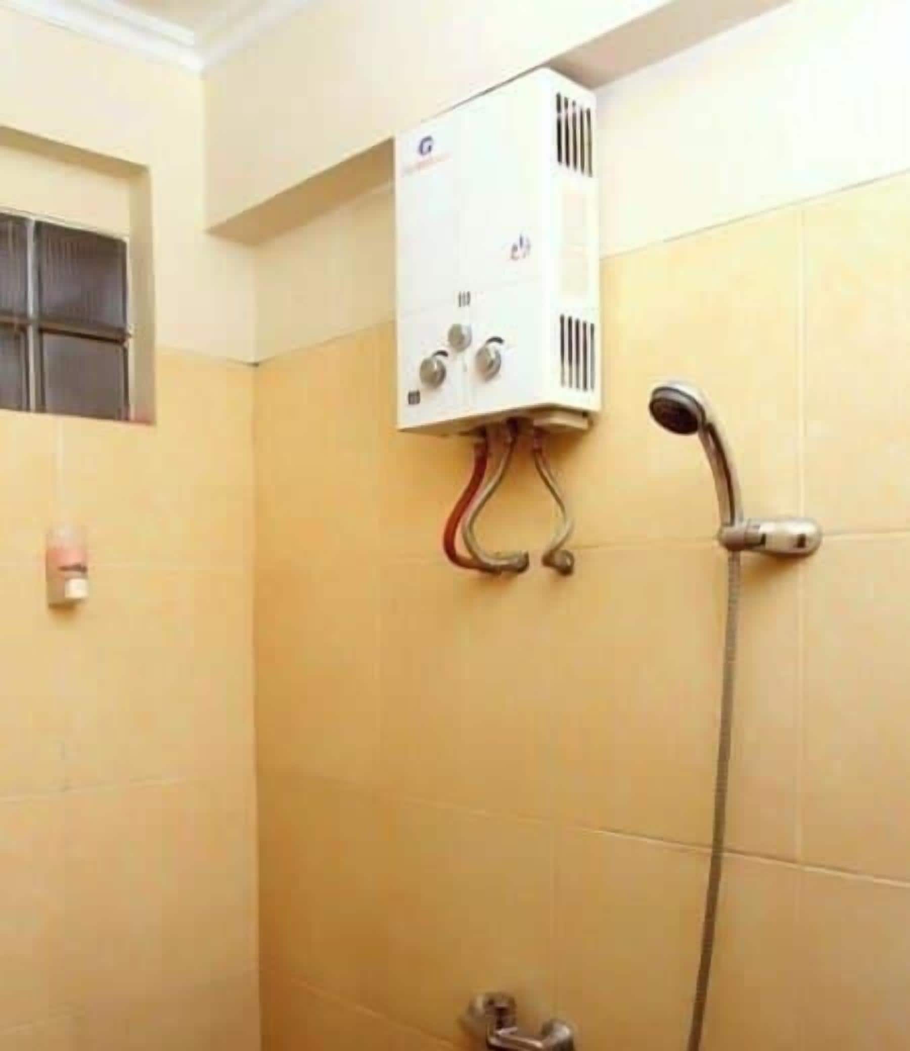 A bathroom with a shower, a wall-mounted heater, and a window with bars.