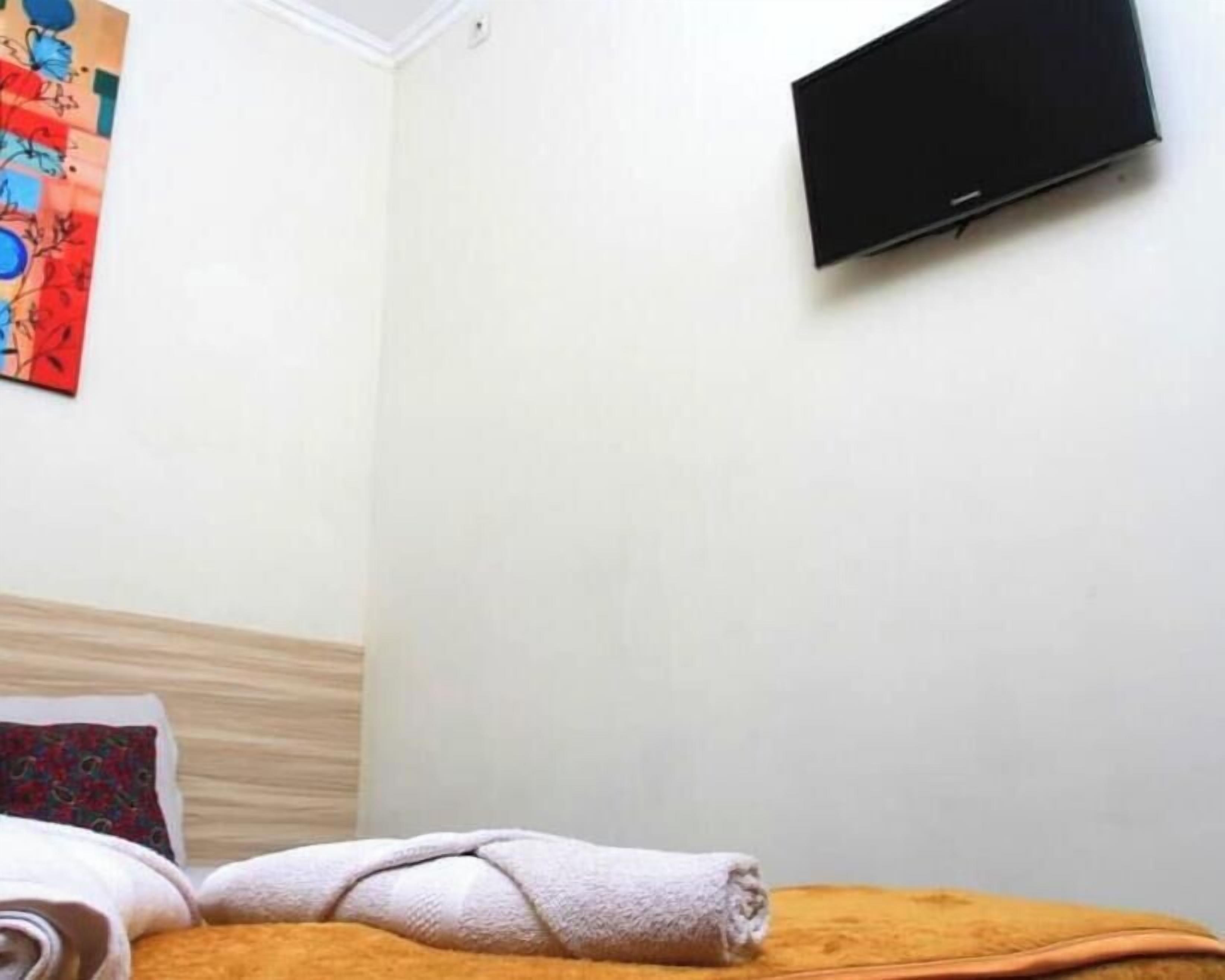 A hotel room with a bed, a wall-mounted TV, and a colorful painting.