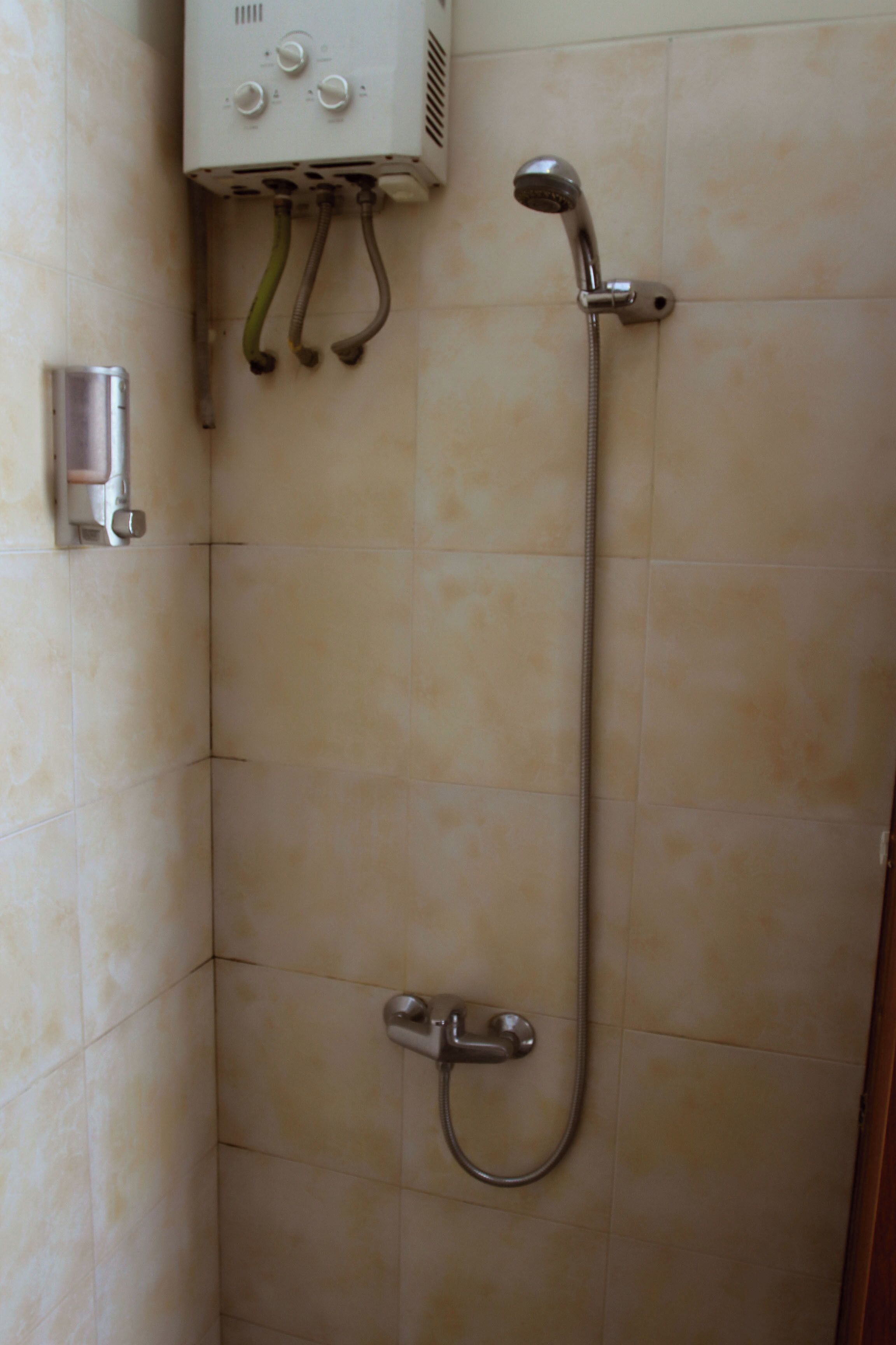 Een douche met een handdouche en een bedieningspaneel aan de muur.