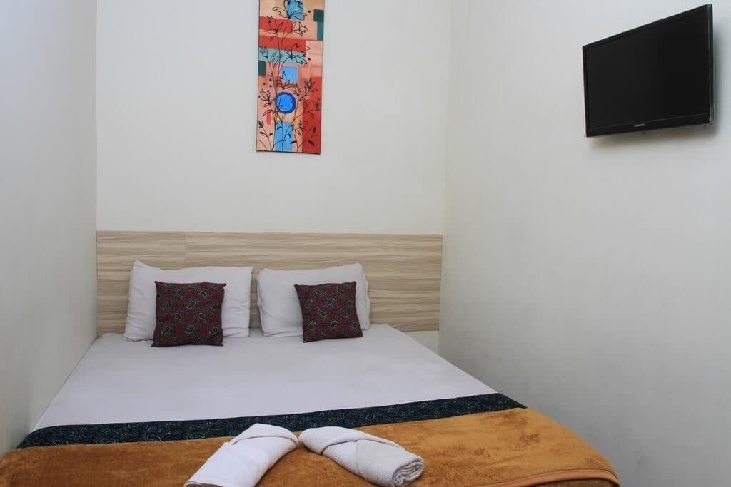 A hotel room with a bed, two pillows, a blanket, and a TV mounted on the wall.