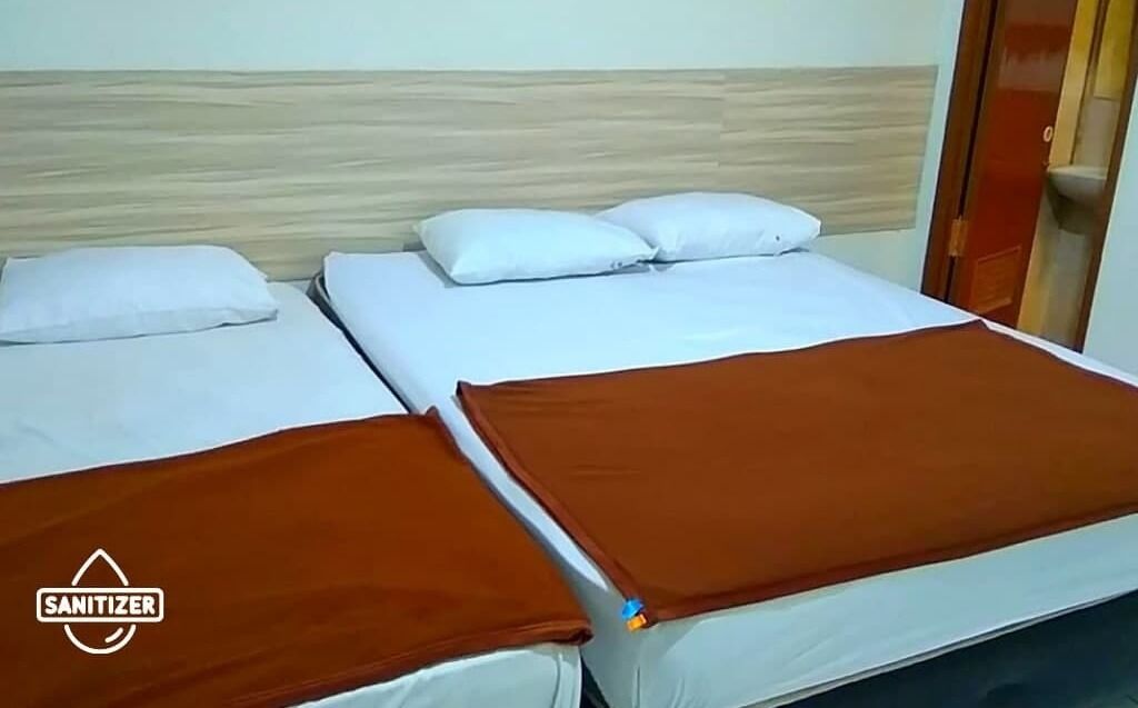A room with two beds, each with white bedding and brown blankets.