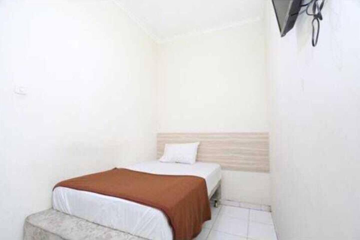 Ein kleines Zimmer mit einem Einzelbett, einem Holz-Kopfteil, einer weißen Bettdecke und einer braunen Decke.