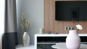 A modern living room with a flat-screen TV mounted on the wall, a white console table, and two vases with flowers. - Vortex Suite KLCC by Idaris (Kuala Lumpur)