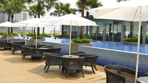 A rooftop pool area with lounge chairs and umbrellas, surrounded by palm trees and modern buildings. - Vortex Suite KLCC by Idaris (Kuala Lumpur)