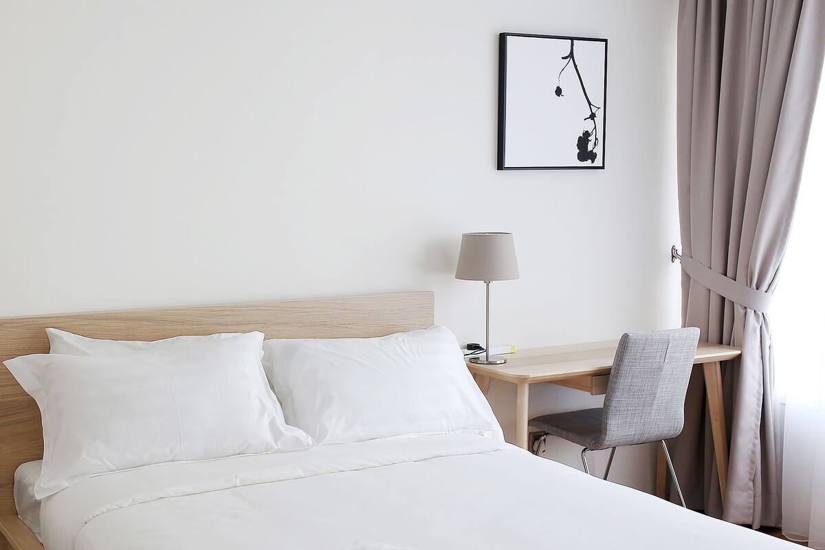 A hotel room with a bed, a desk, a chair, a lamp, and a window with curtains.