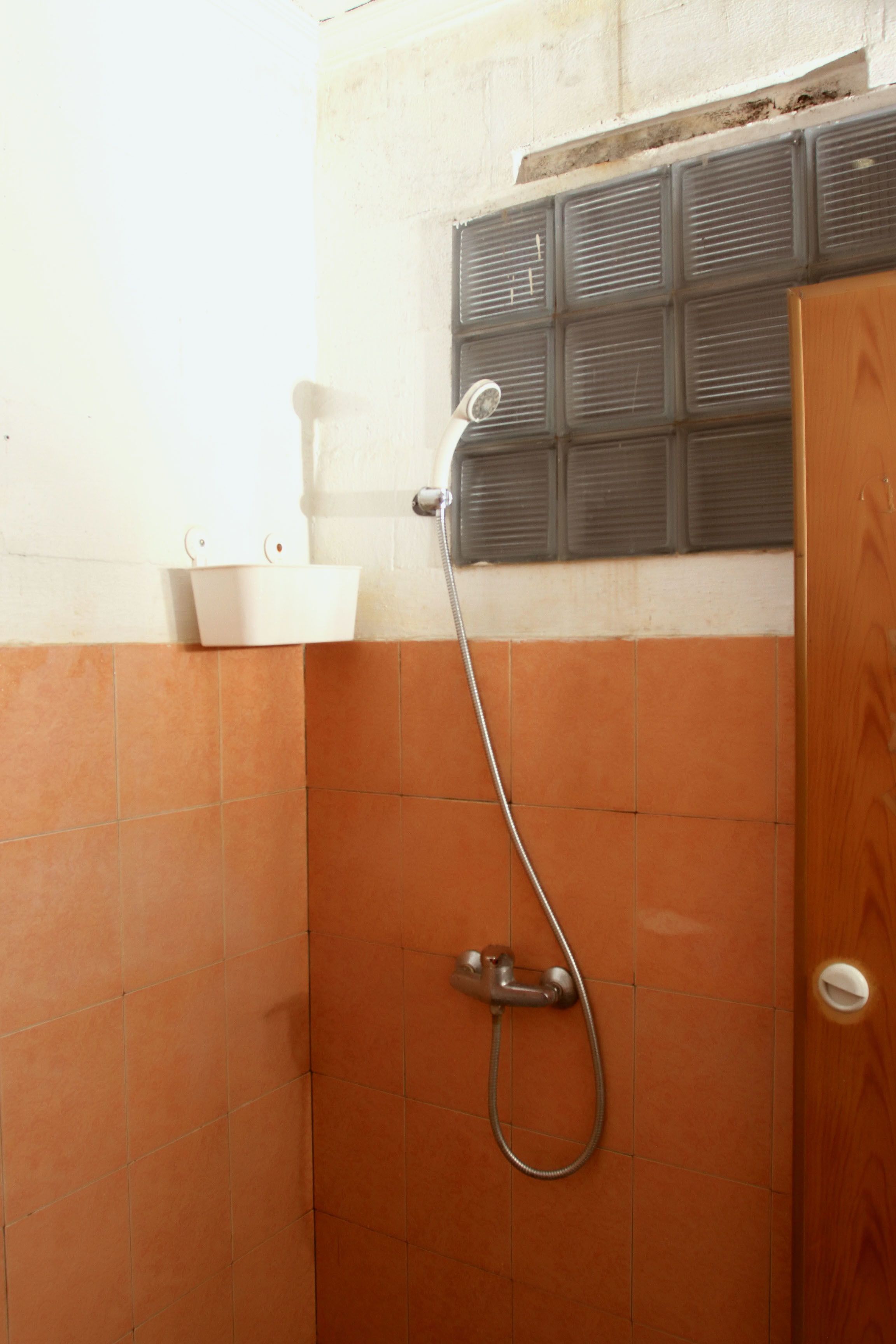 A shower area with orange tiles, a white sink, and a showerhead mounted on the wall.