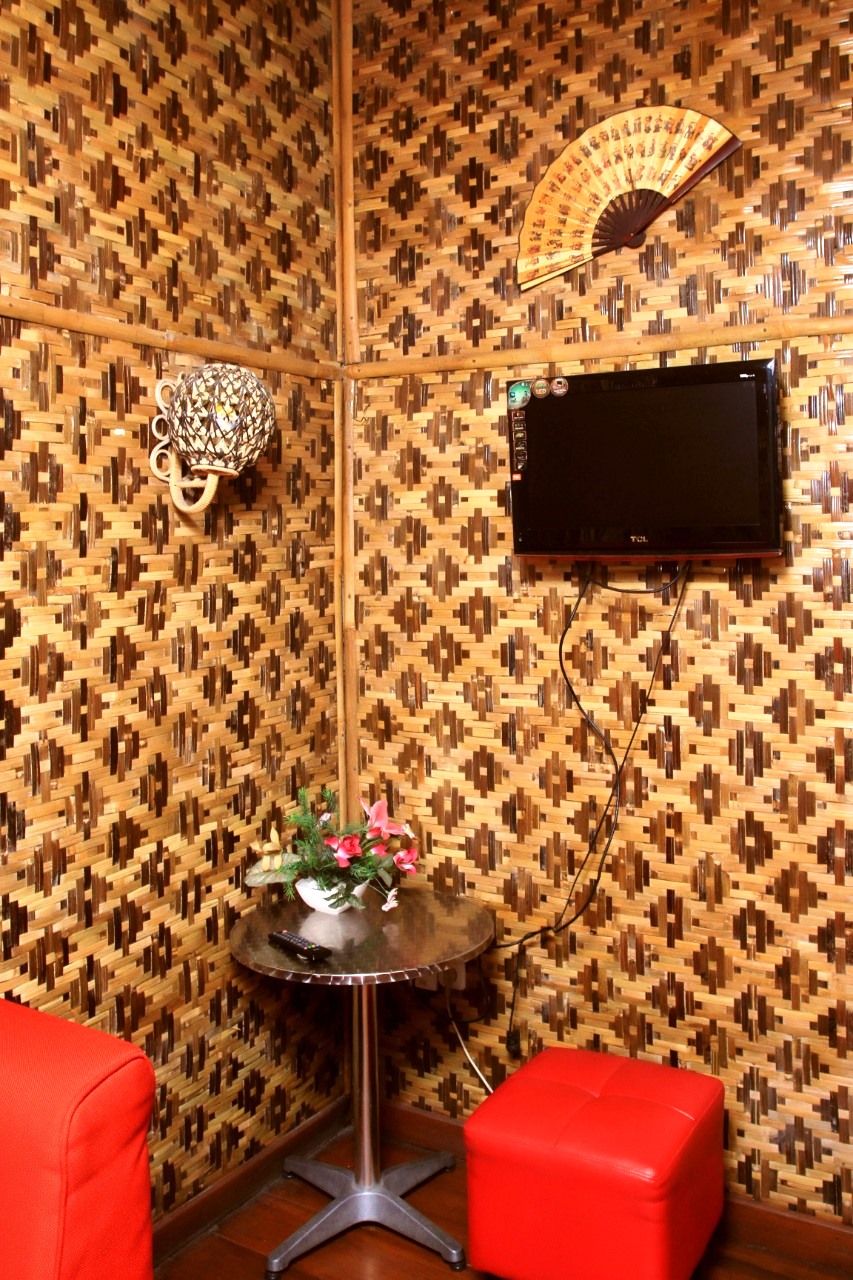 A room with a patterned wall, a flat-screen TV mounted on the wall, a small round table with a vase of flowers, and a red ottoman.