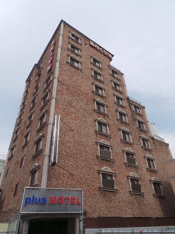 A tall brick building with multiple windows and a sign for Plus Motel.