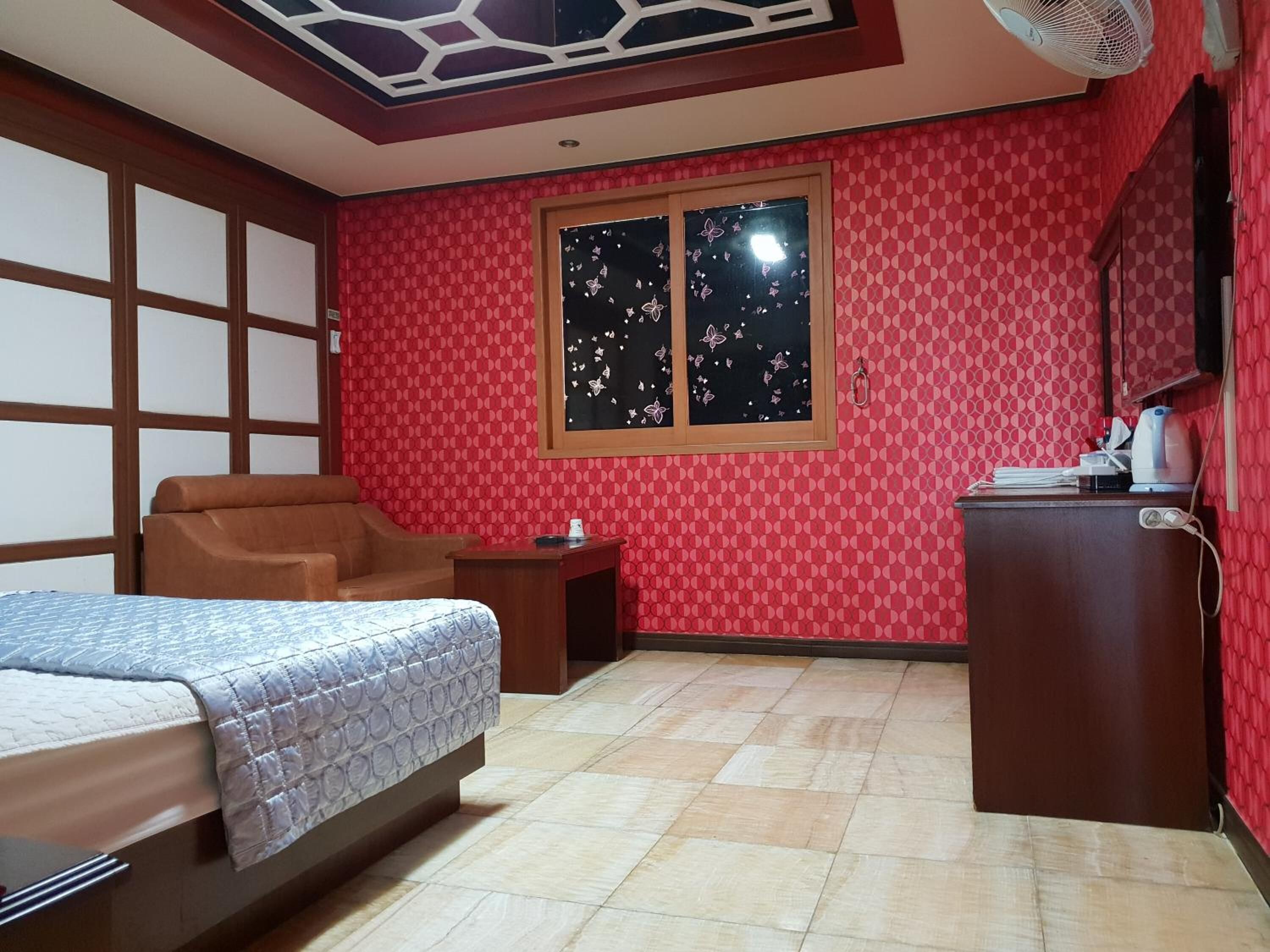 Un dormitorio con cama, una silla, una mesita, una ventana decorada con mariposas y un ventilador de techo.