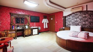 A bedroom with a large bed, a dresser, a desk, a mirror, and a television. - Plus Motel (Busan)