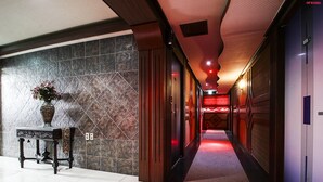 A hotel corridor with a marble wall, a wooden door, and a red-lit hallway. - Plus Motel (Busan)