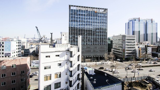 A modern urban landscape with a prominent glass building, a parking lot, and surrounding mid-rise buildings. - Plus Motel (Busan)