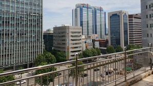A cityscape with modern high-rise buildings, including a prominent glass-fronted structure and a building with a sign reading "ALL NEW CRUZE". - Plus Motel (Busan)