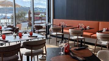 Un restaurante con mesas y sillas, vistas al puerto y un ventanal grande.