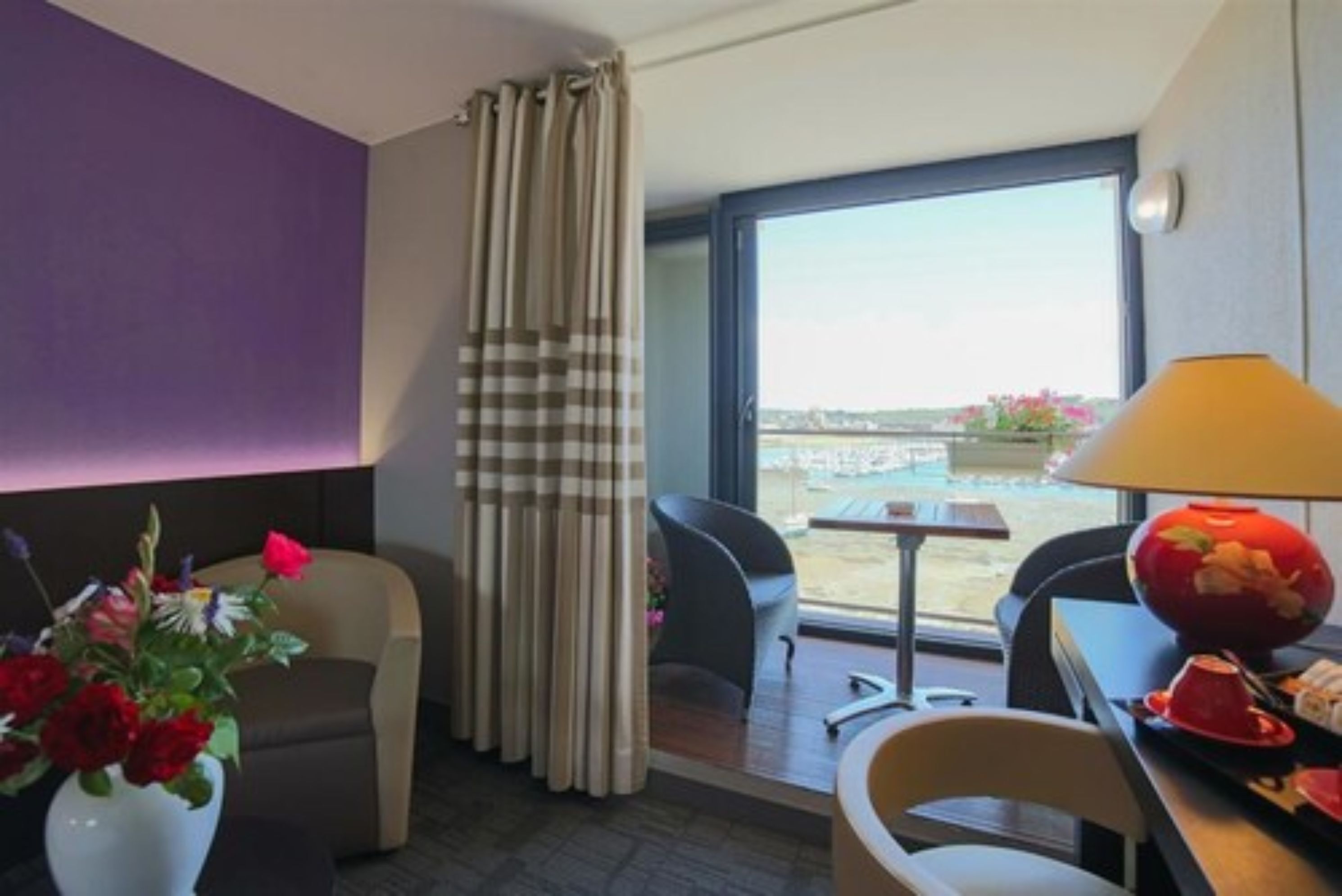 A hotel room with a view of the city, a dining area, and a window with curtains.