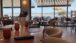 A restaurant with large windows, tables, chairs, and a view of the marina.